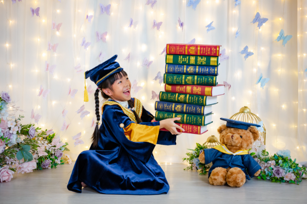 young child with graduation gown holding books