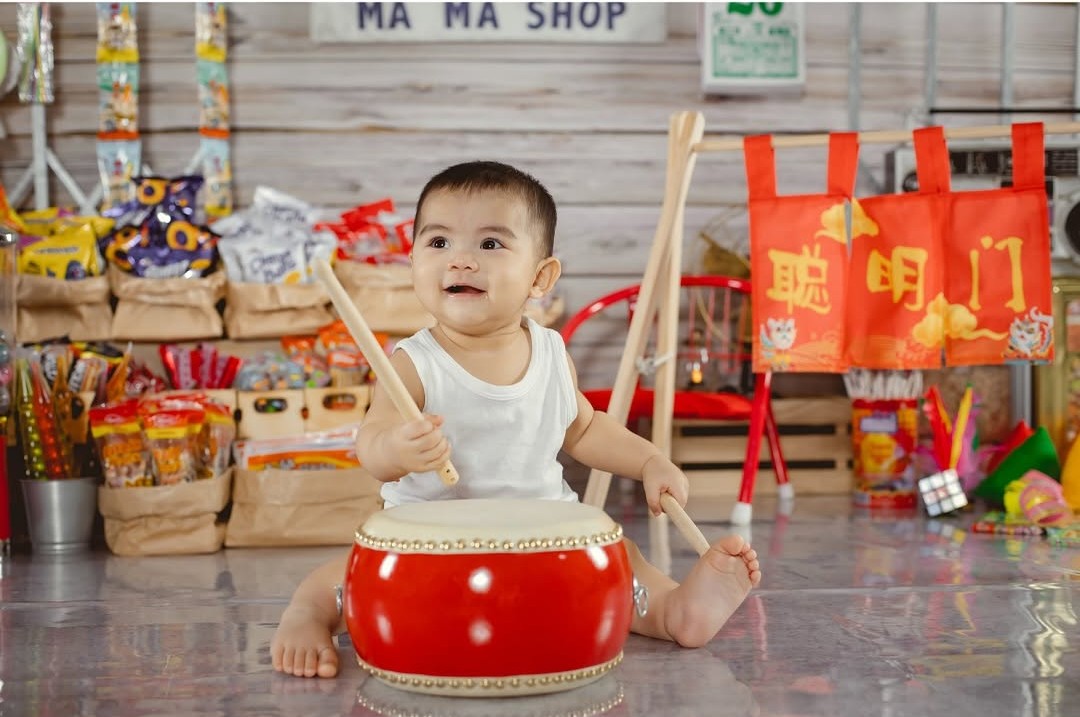 Baby playing with a drum and holding two stick.