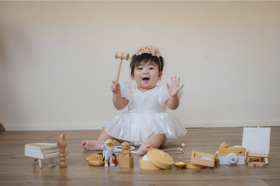 a baby girl picking up a wooden toy gavel on the air while she is sitting on the floor
